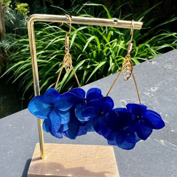 Boucles d’oreilles Chris en véritables hortensias bleu profond, délicatement montés en forme de goutte. Une pièce lumineuse et aérienne qui sublime chaque mouvement avec élégance naturelle.