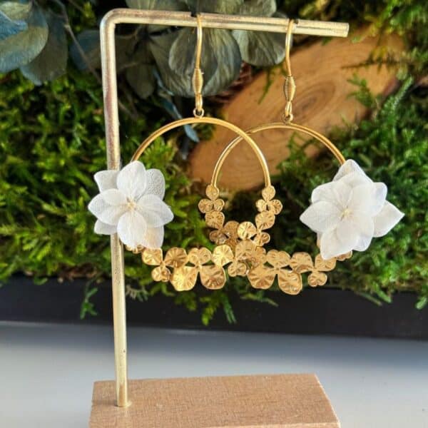 Les boucles d’oreilles Justine associent l’élégance d’un grand anneau doré à la délicatesse de petites fleurs blanches stabilisées. Un bijou floral raffiné et original, parfait pour une mariée ou pour illuminer une tenue avec une touche bohème chic.
